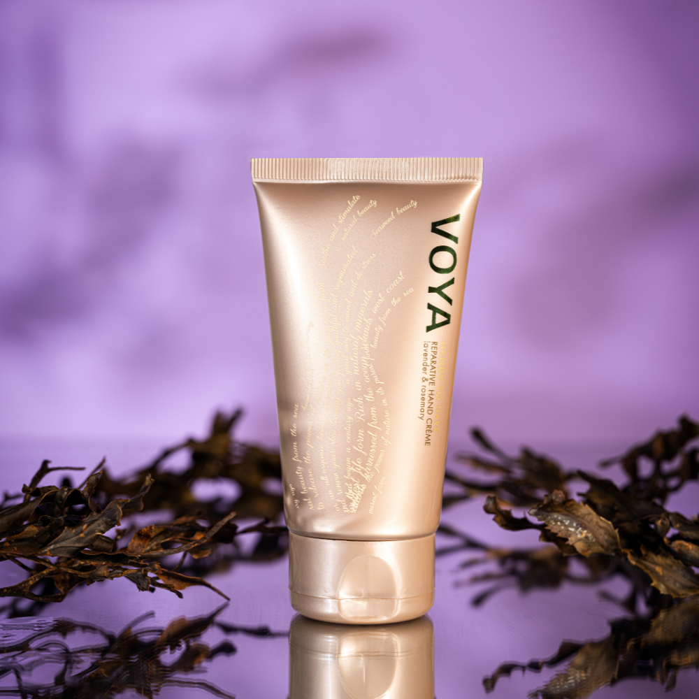 Voya hand cream tube on a reflective surface with a blurred natural background