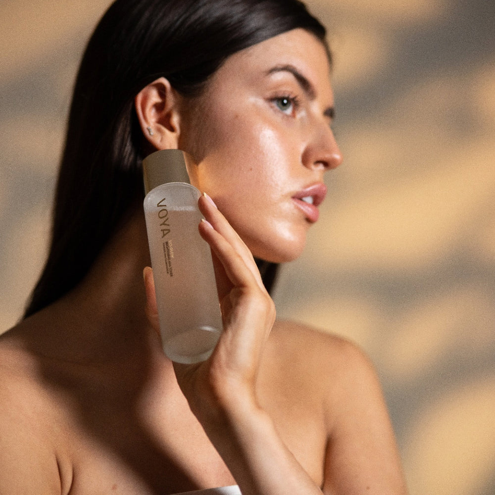 Woman holding a VOYA Bio Glow skincare bottle against her face with a blurred background