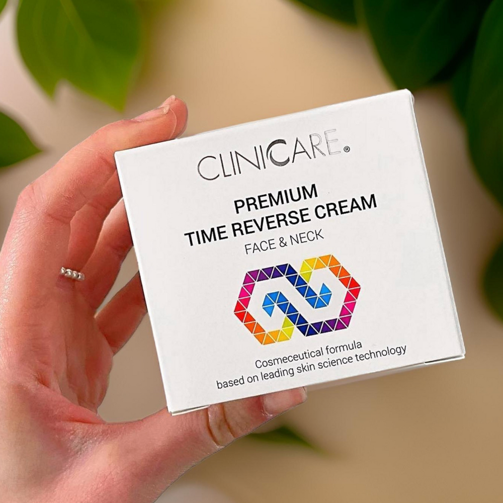 Hand holding ClinicCare Premium Time Reverse Cream box against green foliage background