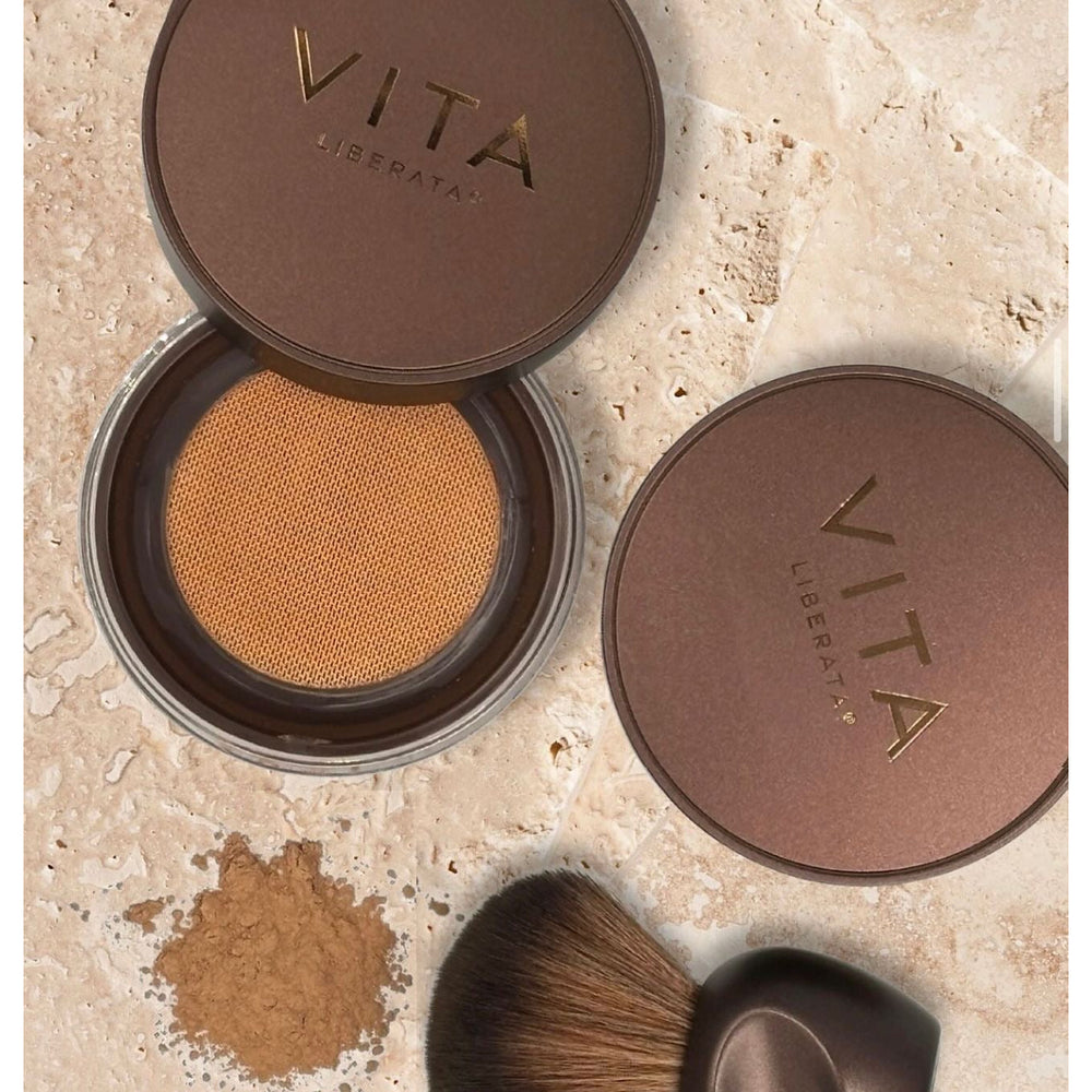 Vita Liberata compact powder with brush on a beige surface