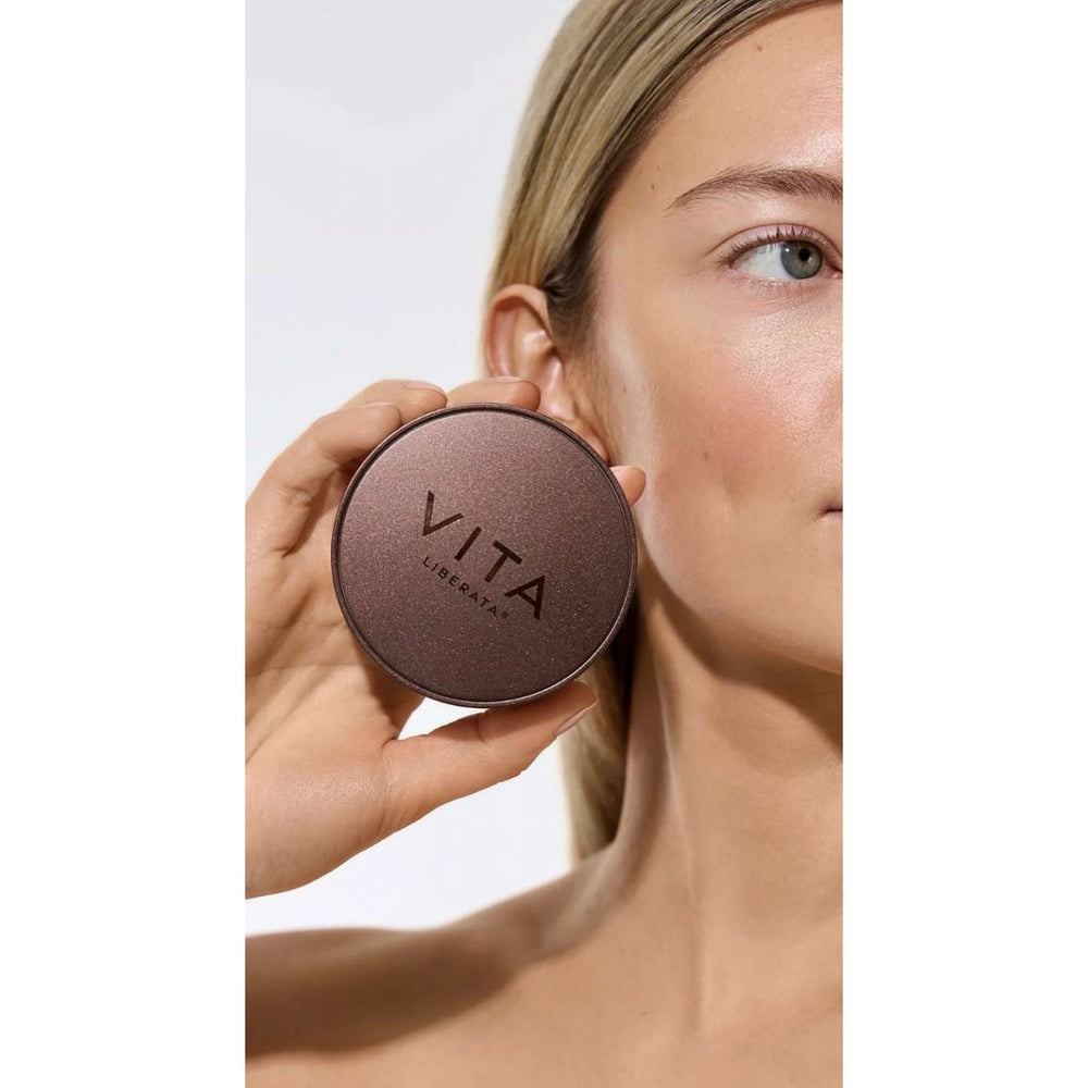 Person holding a round brown compact with 'Vita' branding against a neutral background