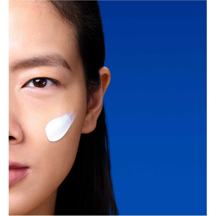 Close-up of a woman's face with La Roche Posay Anthelios Age Correct SPF product application on her cheek against a blue background