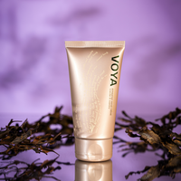 Voya hand cream tube on a reflective surface with a blurred natural background