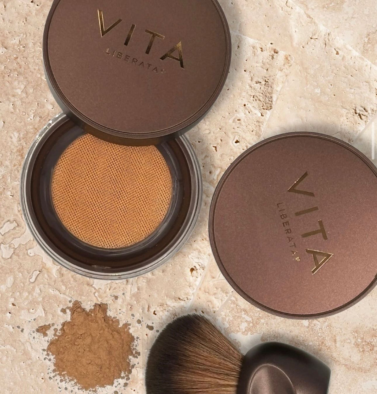 Vita Liberata compact powder with brush on a beige surface