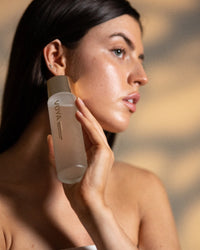 Woman holding a VOYA Bio Glow skincare bottle against her face with a blurred background
