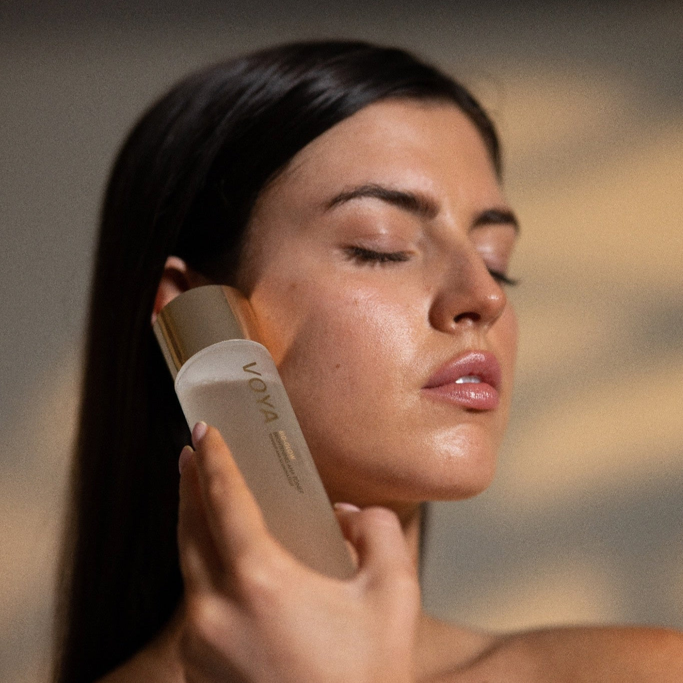 Woman applying VOYA Bio Glow skincare product to her face with a blurred background