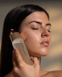 Woman applying VOYA Bio Glow skincare product to her face with a blurred background