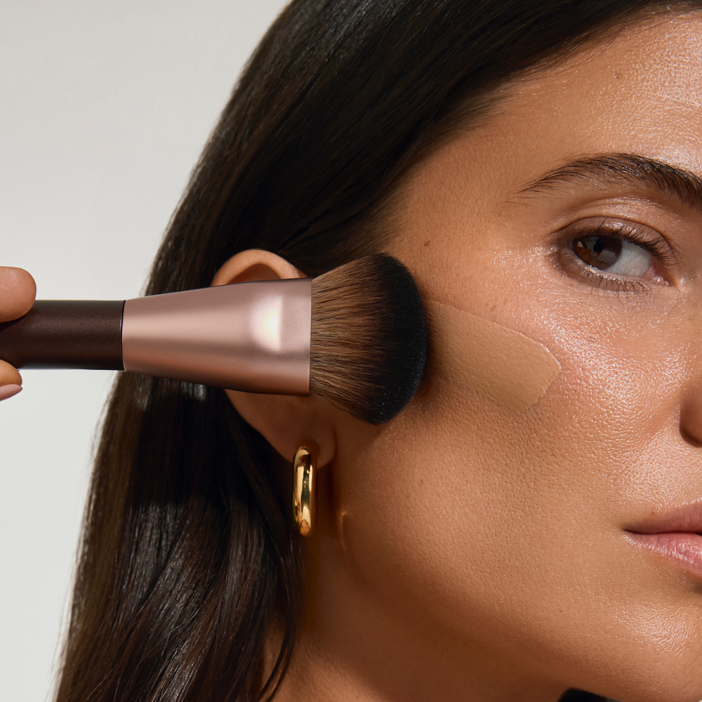 Product photo of the Vita Liberata Face Tan Brush being used by a woman to apply tanning product 