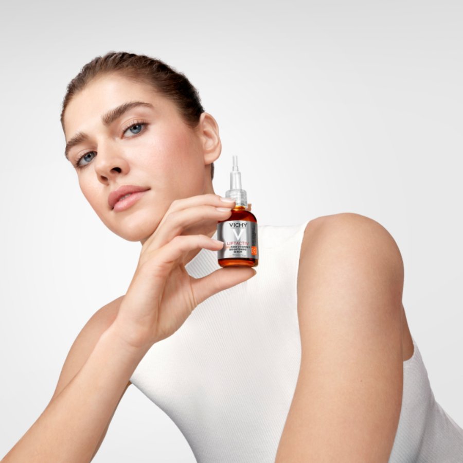 Woman holding a skincare serum bottle with a neutral background