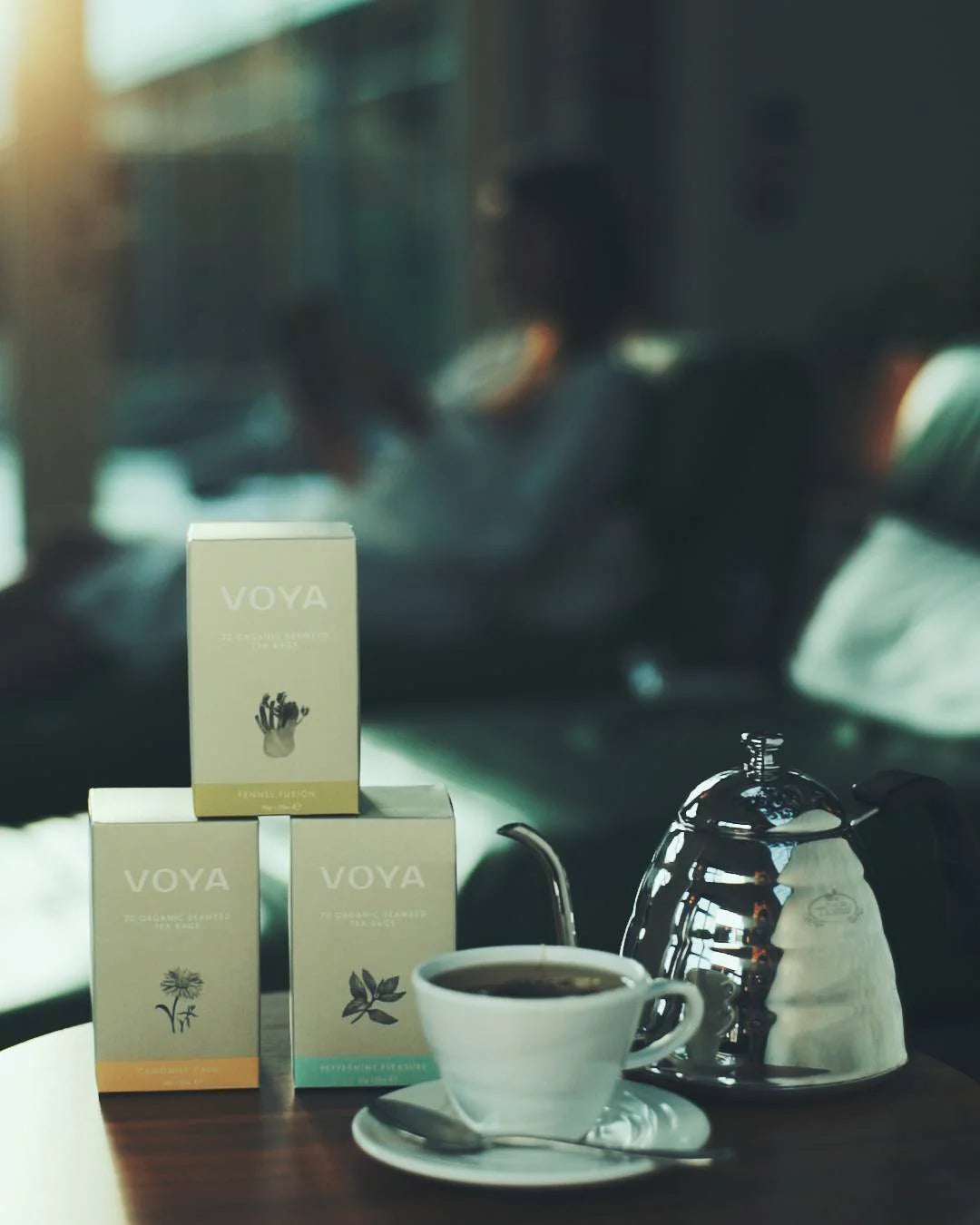 Voya tea boxes with a cup of tea on a table