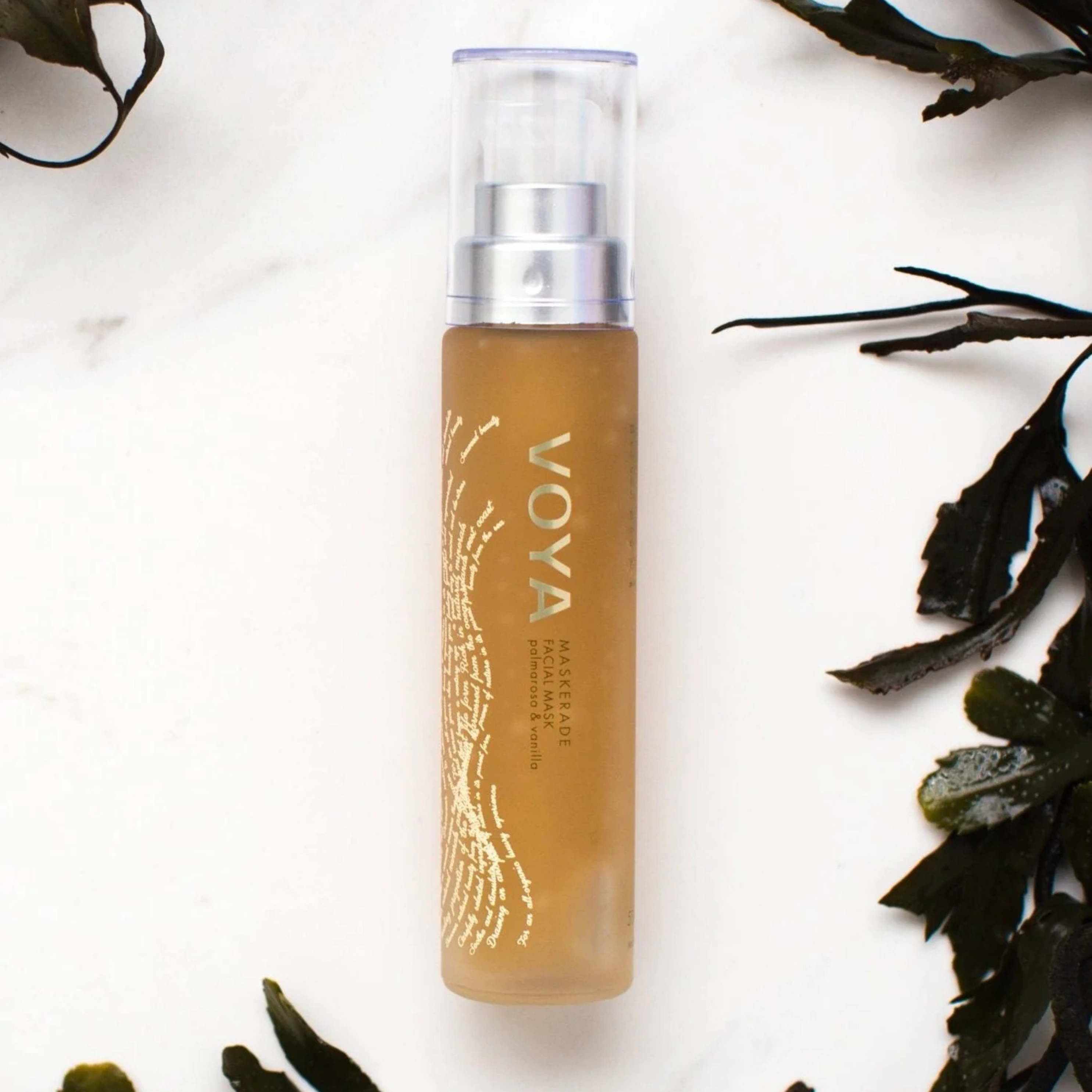 Voya Maskerade Soothing Facial Mask in glass pump bottle with clear lid, hydrating, tightening and brightening.  On a beach with seaweed