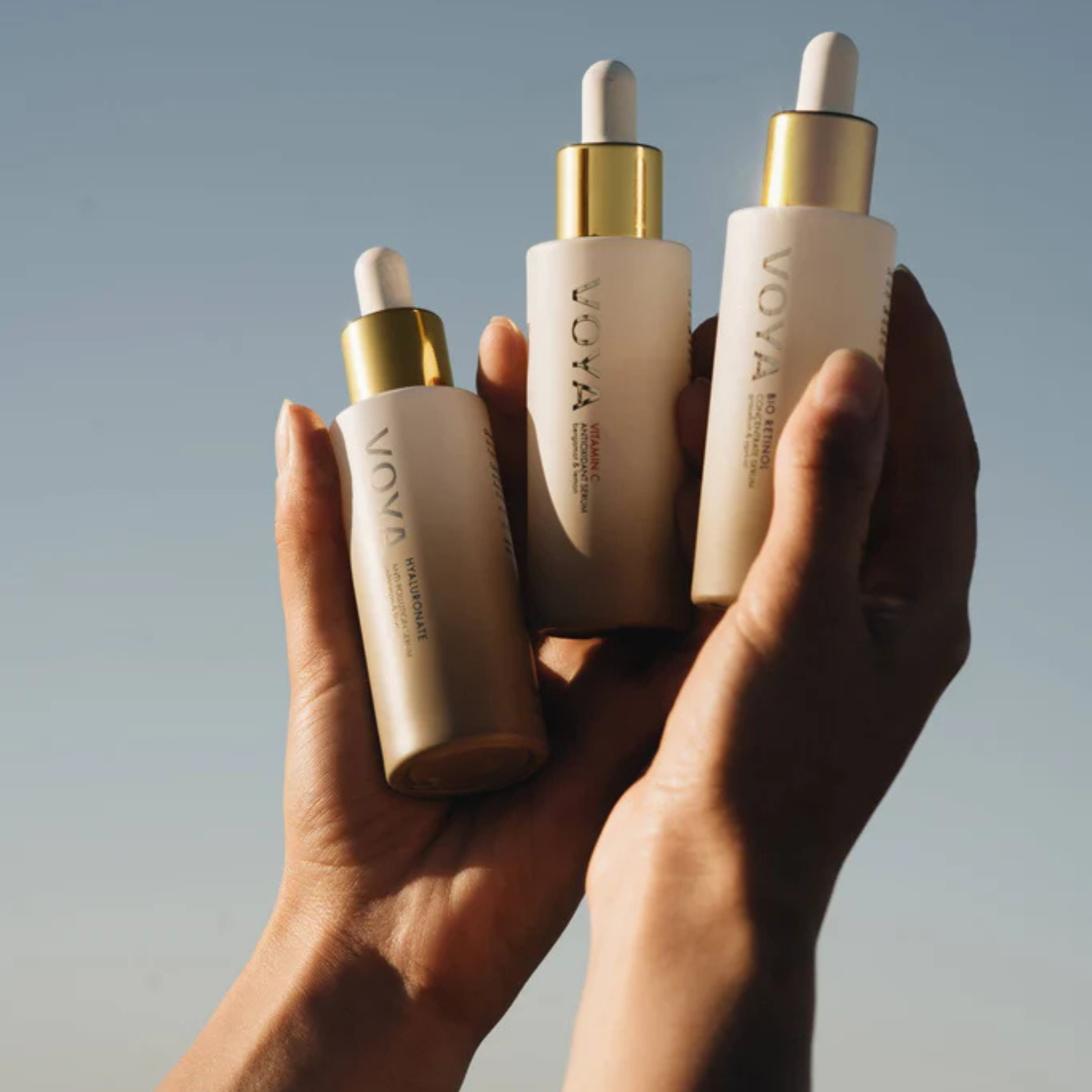 Three VOYA skincare bottles held in a hand against a neutral background