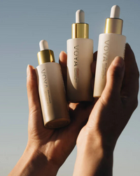 Three VOYA skincare bottles held in a hand against a neutral background