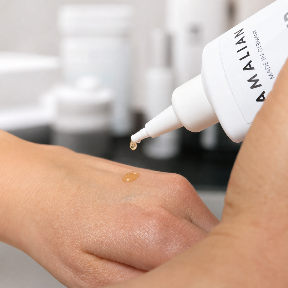 Amalian Hair Growth Booster golden serum being dispensed as a single drop onto the back of a hand, showing its lightweight texture