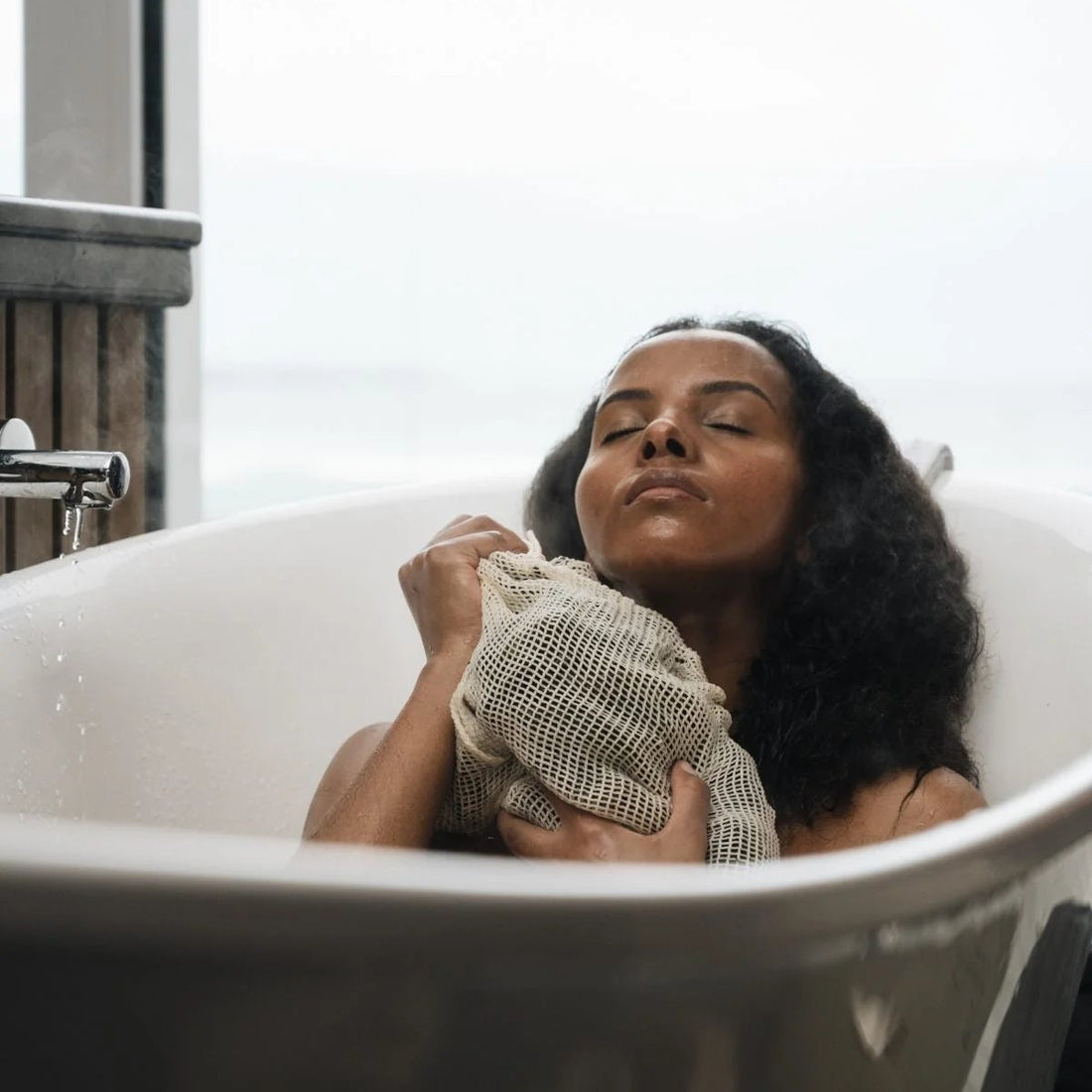 Woman in a bathtub holding a towel, with a neutral background