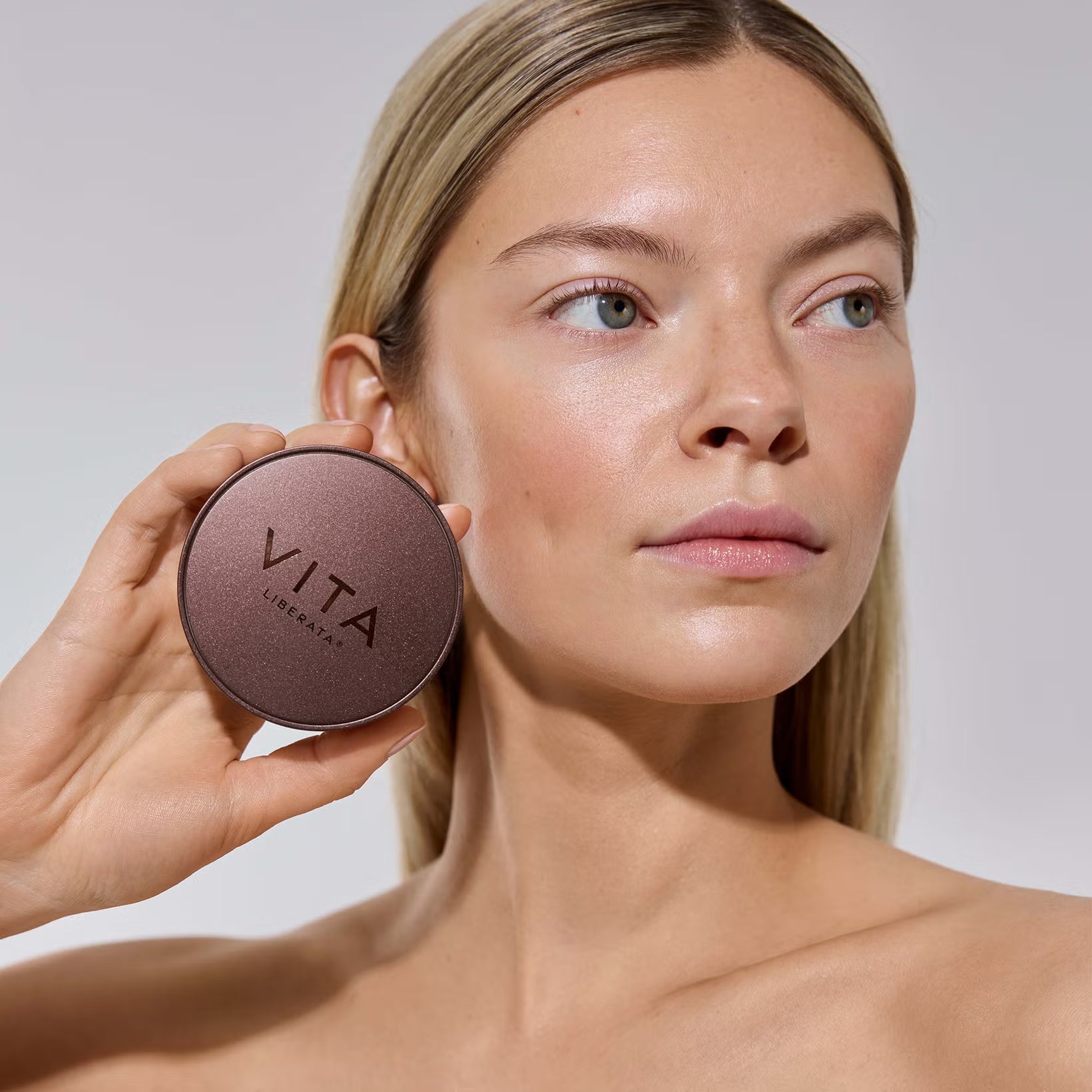 Woman holding a Trystal minerals bronzer with 'Vita' branding against a neutral background