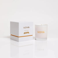 VOYA scented candle in a frosted glass jar next to its white packaging box with gold lettering, set against a clean white background with a soft reflection.
